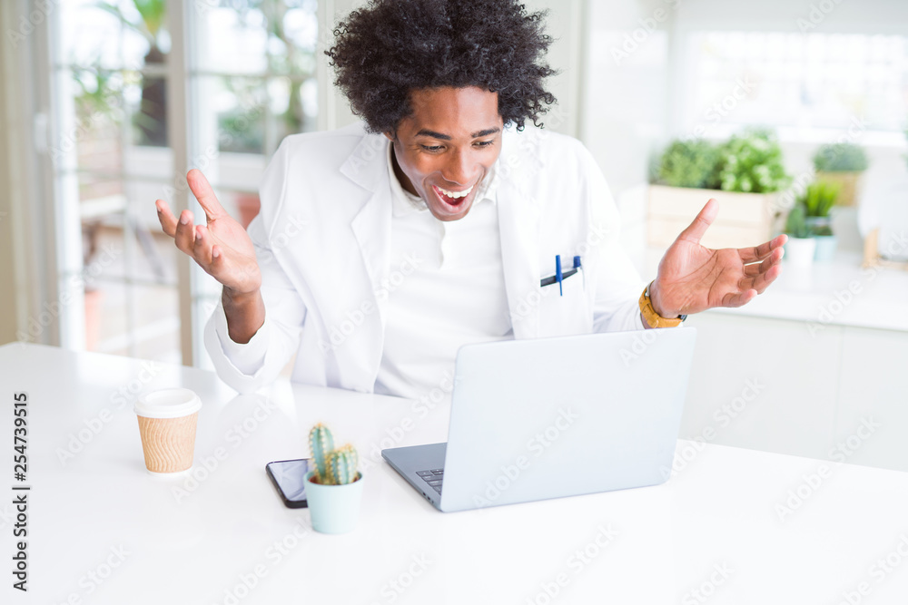 African American doctor man working with laptop at the clinic very happy and excited, winner expression celebrating victory screaming with big smile and raised hands