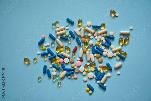 Fototapeta Naklejka Na Ścianę i Meble -  Spilled colored medications and pills on a blue background. Pharmacology and medicine struggle for health. Drug addiction. Treatment of various diseases