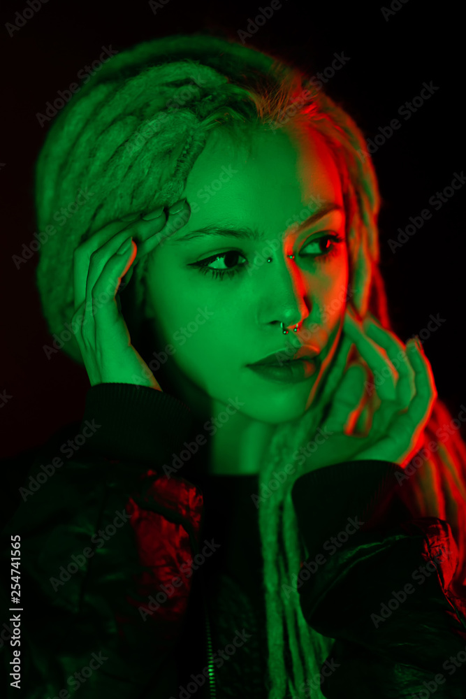 Beautiful girl with dreadlocks and piercings. In the light of the multi-colored  light of green and red portrait on a black background. with hands around  face. color light portrait Stock Photo