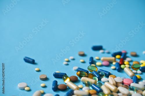 Spilled colored medications and pills on a blue background. Pharmacology and medicine struggle for health. Drug addiction. Treatment of various diseases