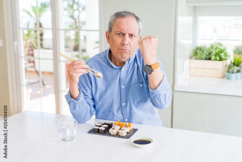 Handsome senior man eating take away sushi using chopsticks at home annoyed and frustrated shouting with anger, crazy and yelling with raised hand, anger concept Handsome senior man eating take away sushi using chopsticks at home annoyed and frustrated shouting with anger, crazy and yelling with raised hand, anger concept