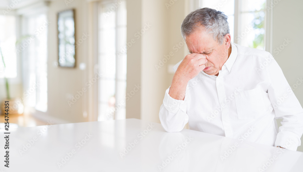 Handsome senior man at home tired rubbing nose and eyes feeling fatigue and headache. Stress and frustration concept.