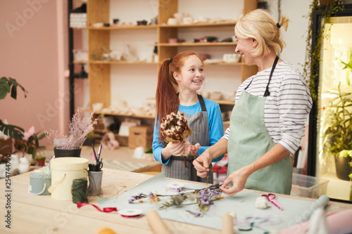 Waist up portrait of smiling mature woman creating flower compositions with teenage girl in art studio, copy space