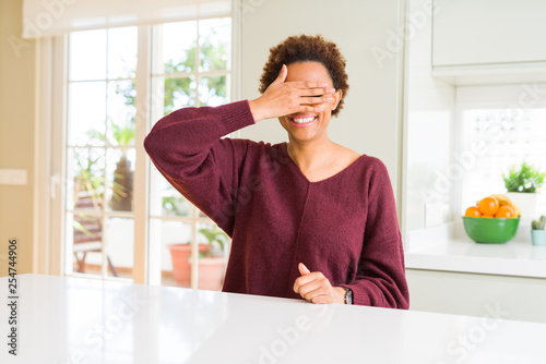 Young beautiful african american woman at home smiling and laughing with hand on face covering eyes for surprise. Blind concept.