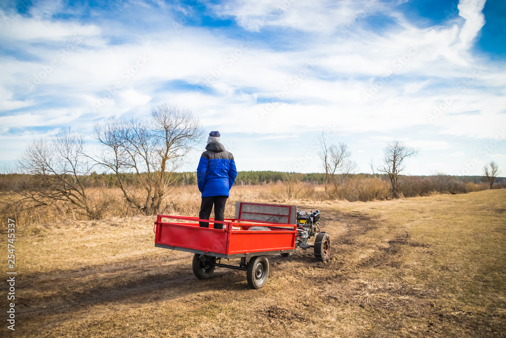 Obraz premium A man on a motoblock rides a field road in spring in March