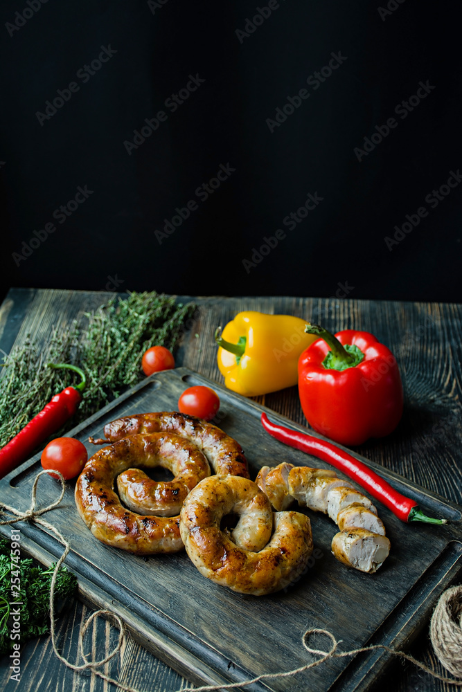 Fried sausage with herbs and spices, wooden background. Ring of baked homemade sausage. Served on a wooden board with greens and vegetables. Side view.