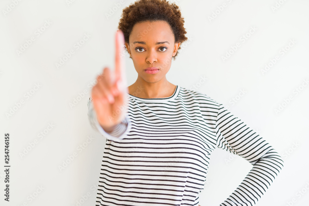 Young beautiful african american woman wearing stripes sweater over white background Pointing with finger up and angry expression Young beautiful african american woman wearing stripes sweater over white background Pointing with finger up and angry expression