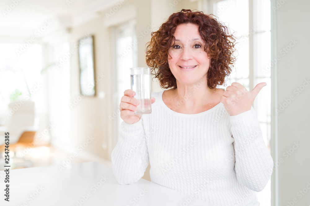 Senior woman driking a fresh glass of water pointing and showing with thumb up to the side with happy face smiling Senior woman driking a fresh glass of water pointing and showing with thumb up to the side with happy face smiling