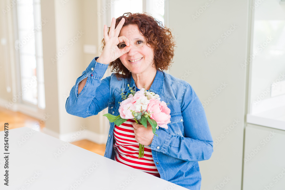 Senior woman holding beautiul bouquet of pink flowers with happy face smiling doing ok sign with hand on eye looking through fingers Senior woman holding beautiul bouquet of pink flowers with happy face smiling doing ok sign with hand on eye looking through fingers