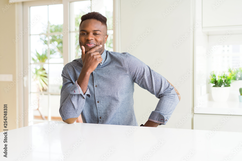 Handsome african american man on white table looking confident at the camera with smile with crossed arms and hand raised on chin. Thinking positive. Handsome african american man on white table looking confident at the camera with smile with crossed arms and hand raised on chin. Thinking positive.