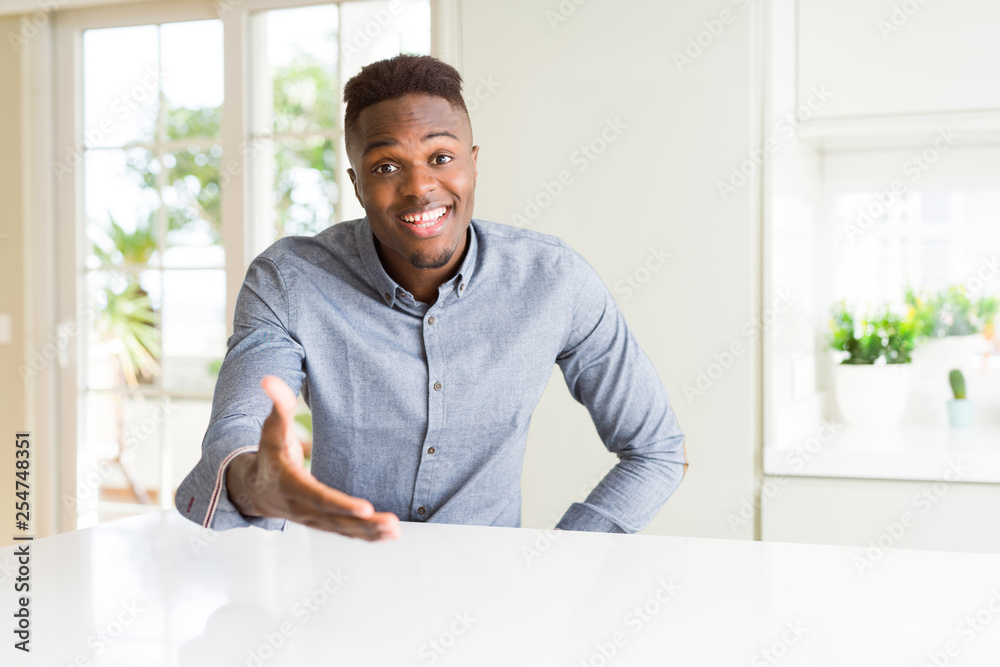 Handsome african american man on white table smiling friendly offering handshake as greeting and welcoming. Successful business.