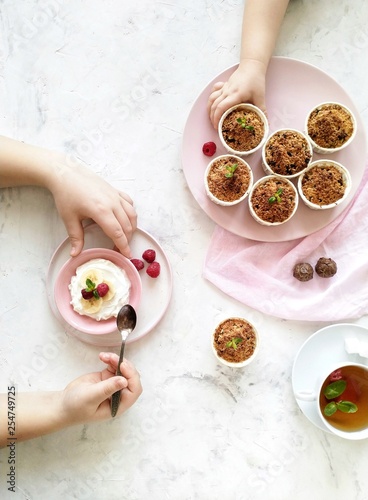 Children's hands holding a spoon and take a muffin from the plate. Muffins, cream with banana and raspberry on a light background top view