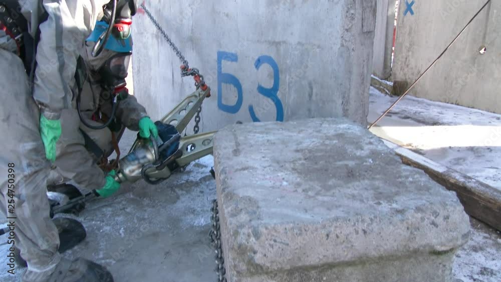 Two people in Khazmat uniforms use a hydraulic tool to move cargo, which prevents them from reaching a dangerous place to analyze the chemical and radiation environment. Analysis of debris. Cleaning t Two people in Khazmat uniforms use a hydraulic tool to move cargo, which prevents them from reaching a dangerous place to analyze the chemical and radiation environment. Analysis of debris. Cleaning t