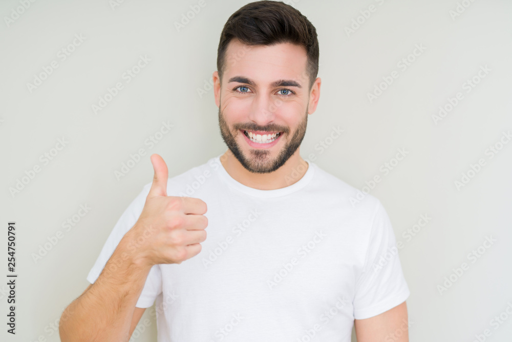 Young handsome man wearing casual white t-shirt over isolated background doing happy thumbs up gesture with hand. Approving expression looking at the camera with showing success. Young handsome man wearing casual white t-shirt over isolated background doing happy thumbs up gesture with hand. Approving expression looking at the camera with showing success.