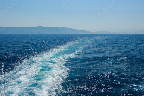Island silhouette in the background. View from a boat with long path of waves from a boat. Deep dark blue water. Mediterranean Sea.