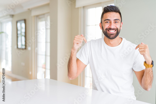 Handsome hispanic man casual white t-shirt at home looking confident with smile on face, pointing oneself with fingers proud and happy.