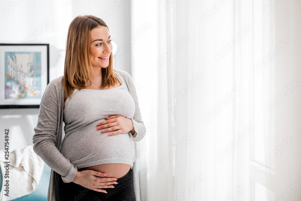 © leszekglasner - Beautiful pregnant woman touching her belly standing by the window at home © leszekglasner - Beautiful pregnant woman touching her belly standing by the window at home