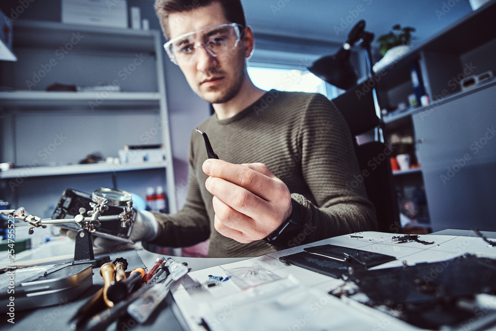 Electronic technician mending a broken phone, looking closely at the little bolt holding it with tweezers in the repair shop