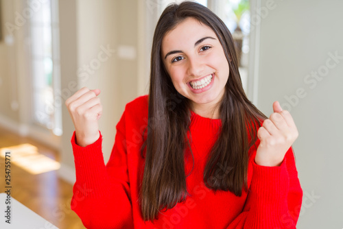 Beautiful young woman wearing casual red sweater celebrating surprised and amazed for success with arms raised and open eyes. Winner concept.