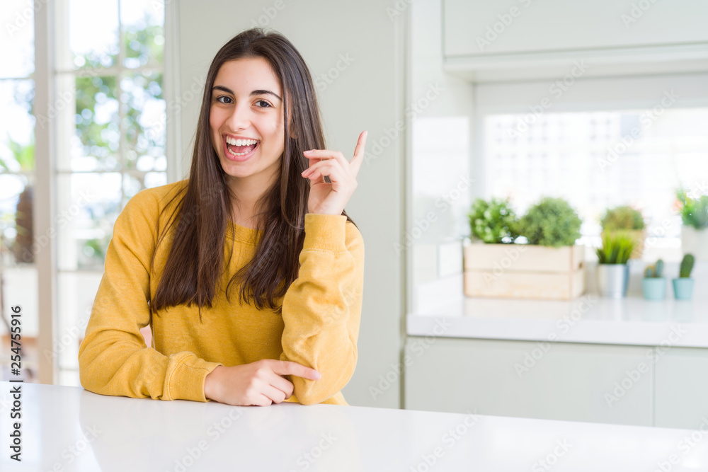 Beautiful young woman wearing yellow sweater with a big smile on face, pointing with hand and finger to the side looking at the camera.