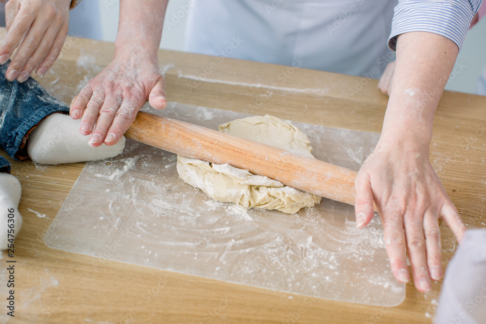 Sheeting dough. Women's hands are holding rolling pin and floured. Hands baking dough with rolling pin. Baking in kitchen. Chef at work. Women at kitchen, little feet of baby on the table