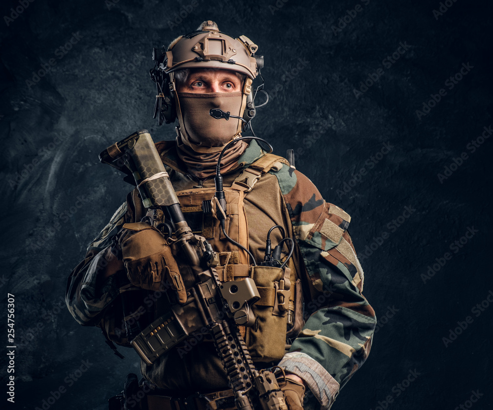 Special forces soldier in military uniform posing with assault rifle. Studio photo against a dark textured wall