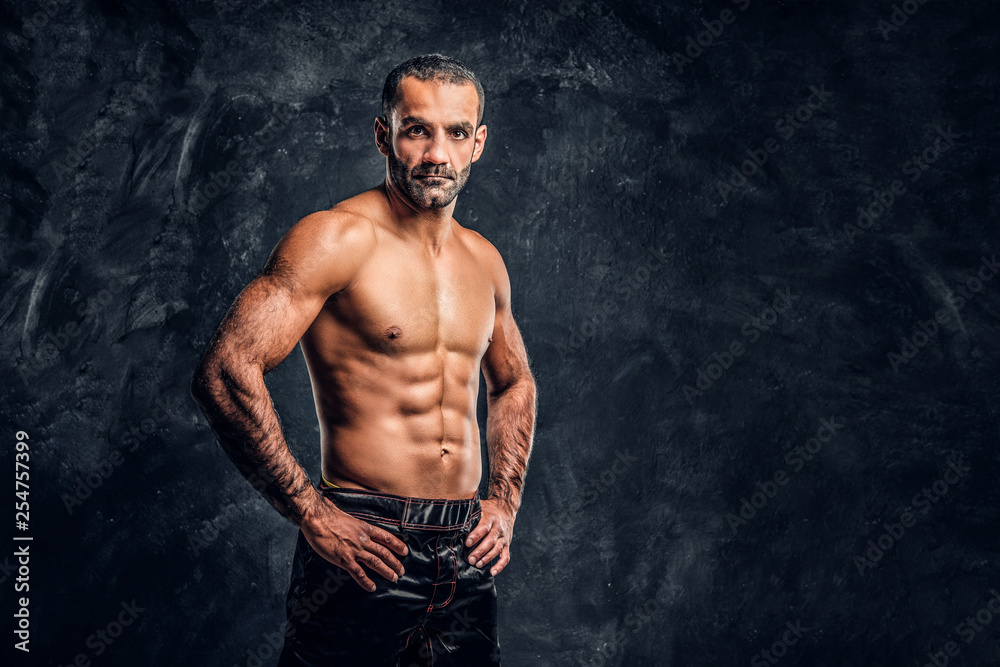 Portrait of a brutal professional fighter with naked torso posing for a camera. Studio photo against a dark textured wall