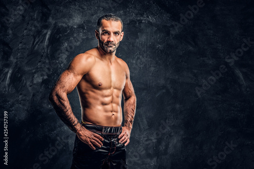 Portrait of a brutal professional fighter with naked torso posing for a camera. Studio photo against a dark textured wall