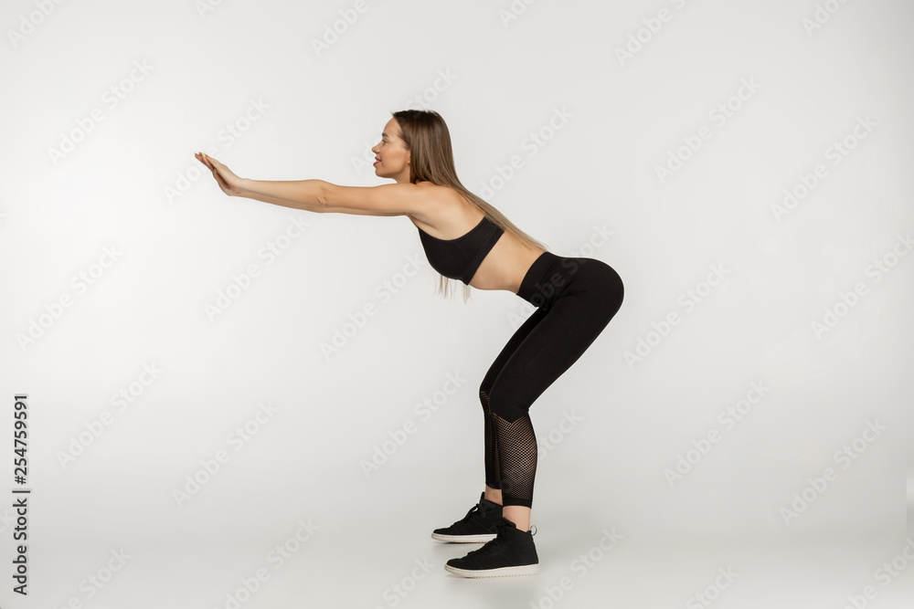 Side view photo of young beautiful woman in black sportswear doing squat exersises