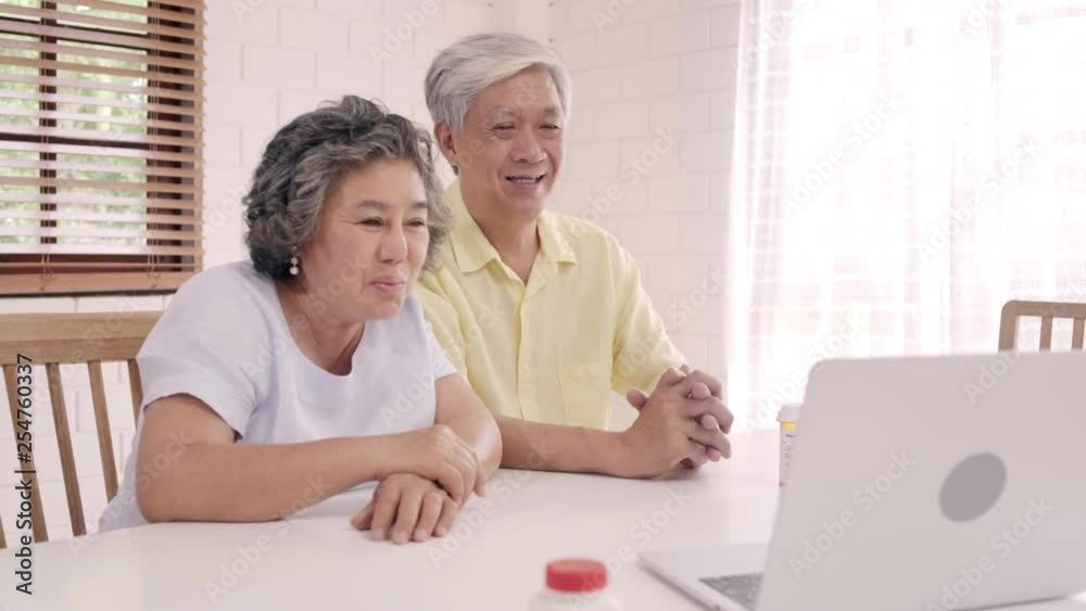 Asian elderly couple using laptop conference with doctor about medicine information in living room, couple using time together while lying on sofa at home. Senior family health at home concept. Asian elderly couple using laptop conference with doctor about medicine information in living room, couple using time together while lying on sofa at home. Senior family health at home concept.