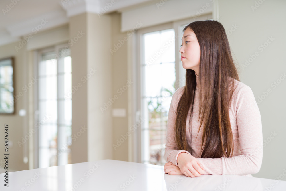 Beautiful Asian woman wearing casual sweater on white table looking to side, relax profile pose with natural face with confident smile. Beautiful Asian woman wearing casual sweater on white table looking to side, relax profile pose with natural face with confident smile.