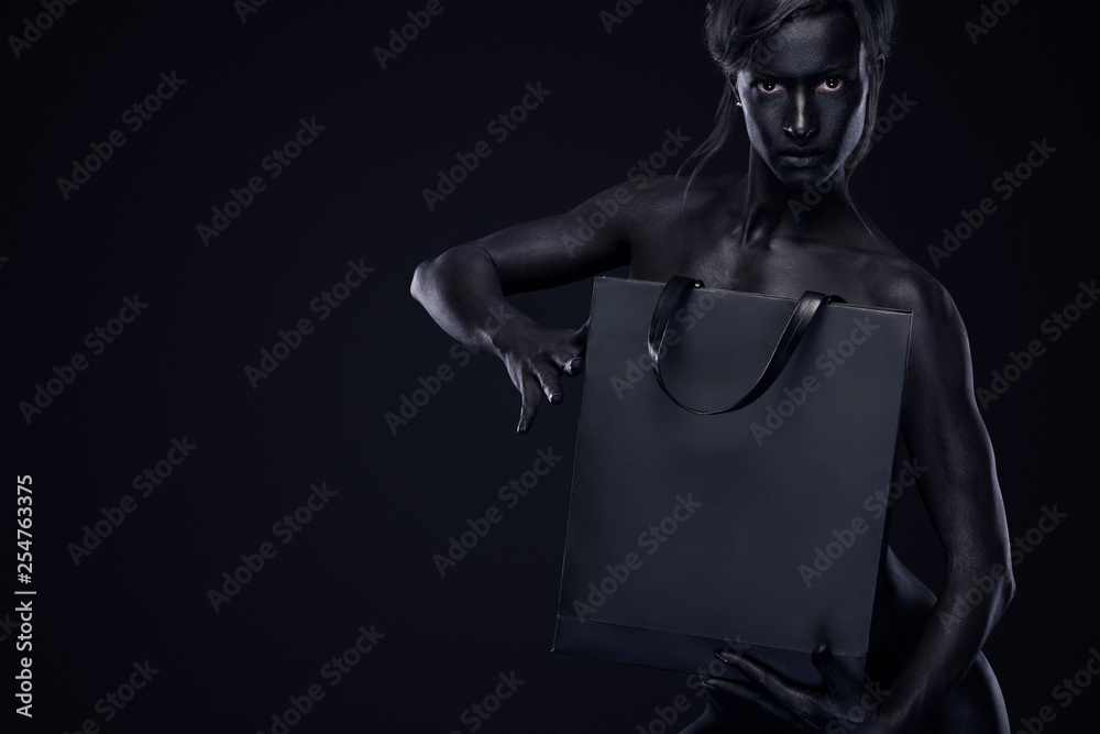 Black friday sale concept. Shopping woman with bodyart and face art holding bag isolated on dark background in holiday. Black friday sale concept. Shopping woman with bodyart and face art holding bag isolated on dark background in holiday.