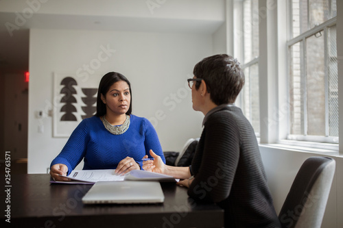 Female colleagues discussing while sitting at desk in office