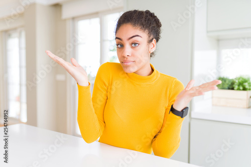 Beautiful young african american woman with afro hair clueless and confused expression with arms and hands raised. Doubt concept.