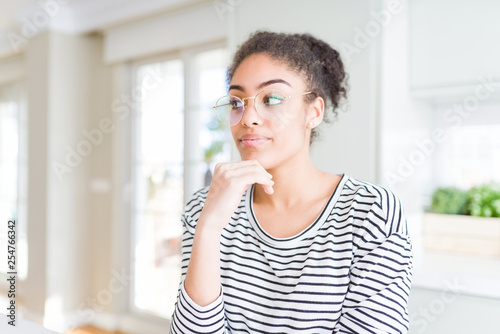 Beautiful young african american woman with afro hair wearing glasses with hand on chin thinking about question, pensive expression. Smiling with thoughtful face. Doubt concept.