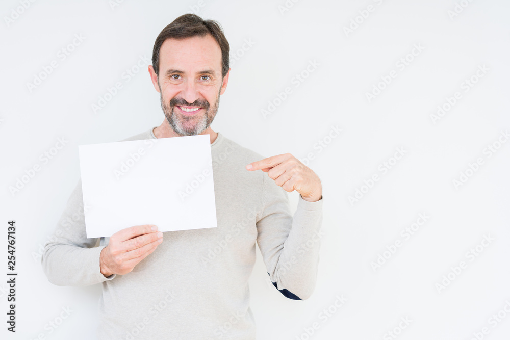 Senior man holding blank paper sheet over isolated background very happy pointing with hand and finger Senior man holding blank paper sheet over isolated background very happy pointing with hand and finger