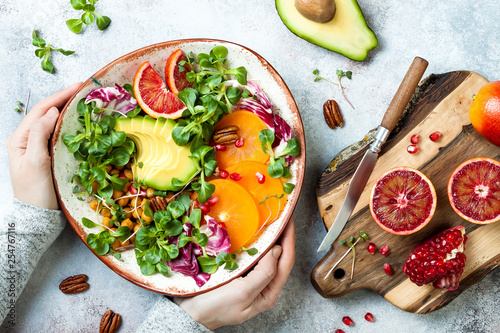 Girl holding vegan, detox Buddha bowl with turmeric roasted  chickpeas, greens, avocado, persimmon, blood orange, nuts and pomegranate. photo