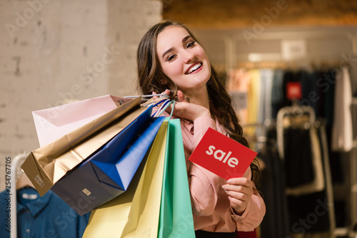 Smiling girl with shopping bags and sale sign.