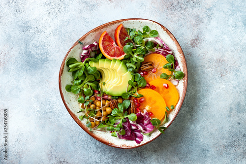 Vegan, detox Buddha bowl with turmeric roasted  chickpeas, greens, avocado, persimmon, blood orange, nuts and pomegranate. Top view, flat lay, copy space photo