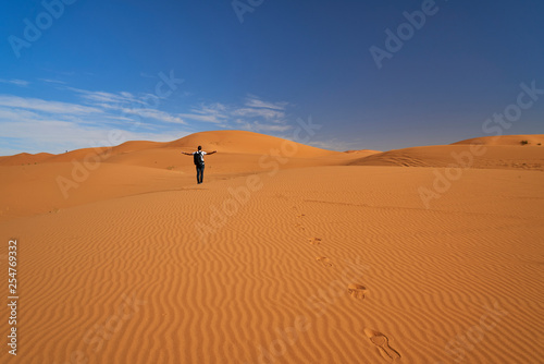 Morocco, back view of man with backpack standing on desert dune