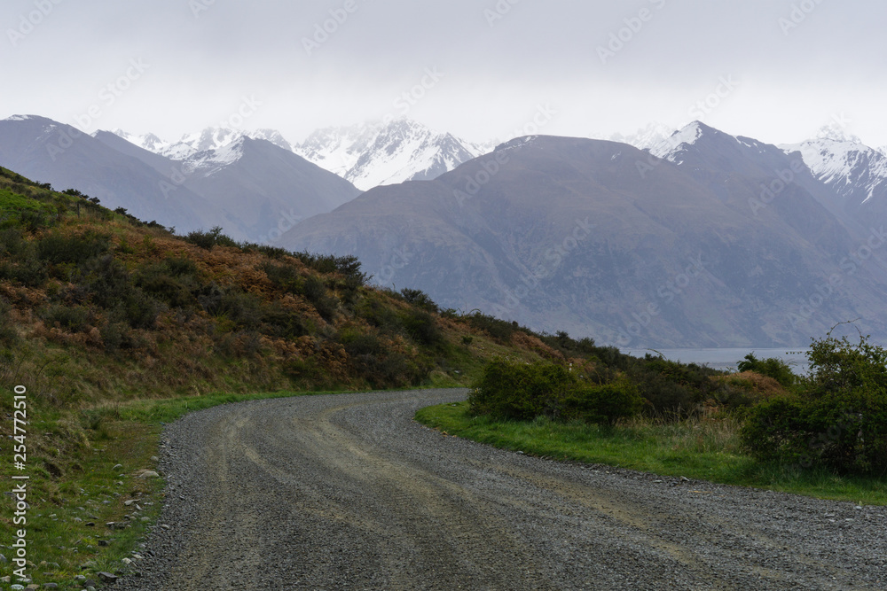 foggy landscape in the mountains, brown hills and peaks covered by snow, road in the valley