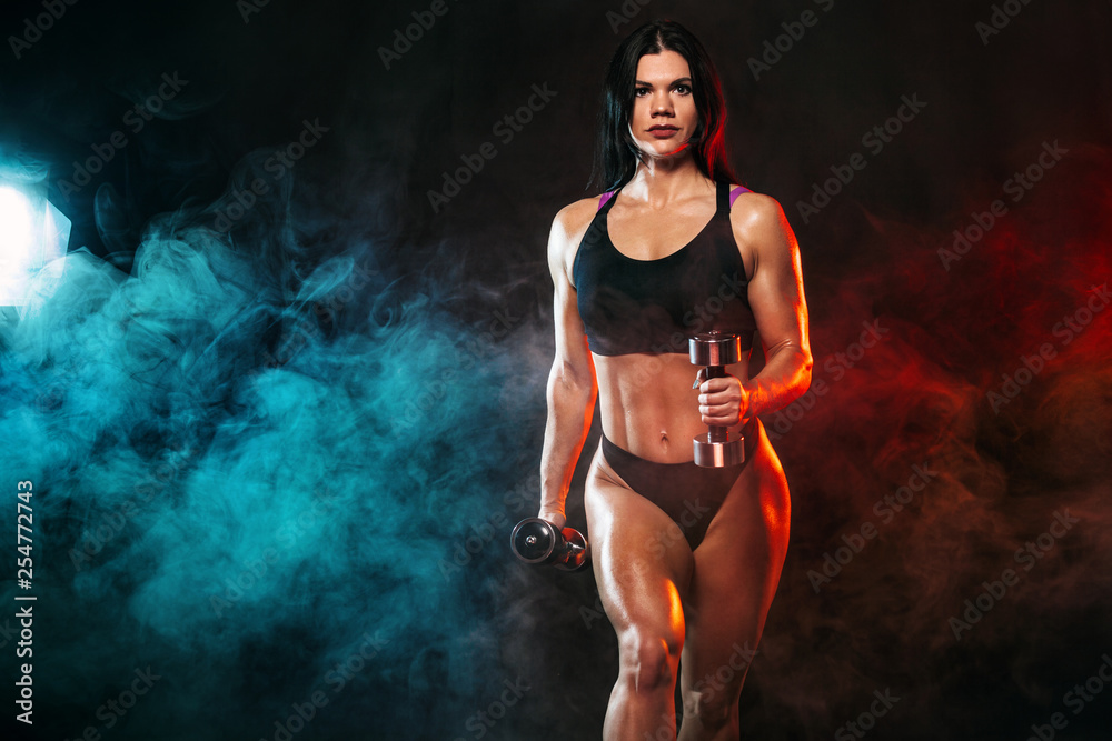 Obraz premium Sporty fit woman, athlete with dumbbells make fitness exercises on black background.