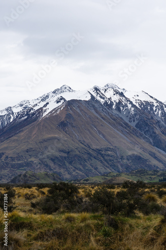 Mountain peak covered with snow, brown hill and dramatic sky