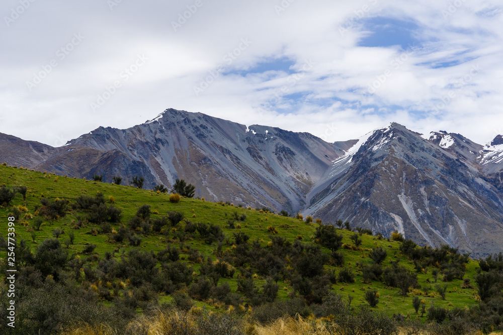 Mountain peak covered with snow, green hill and dramatic sky