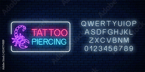 Tattoo and piercing parlor glowing neon signboard with scorpio emblem and alphabet. Tattooing salon sign