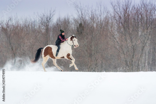 young woman riding her horse through snow bareback on a winter day