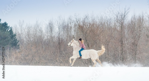 blonde young woman riding her horse through snow bareback on a winter day