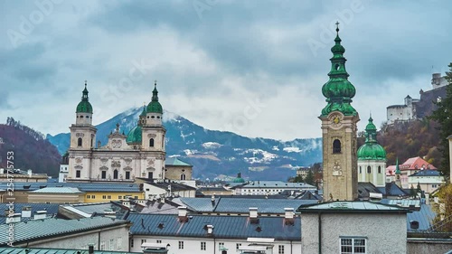 The slope of Monchsberg hill overlooks the roofs of old town, Baroque facade of Salzburg Cathedral, tall belfry of St Peter's Abbey and rainy clouds, havering on mountains, Austria.  photo