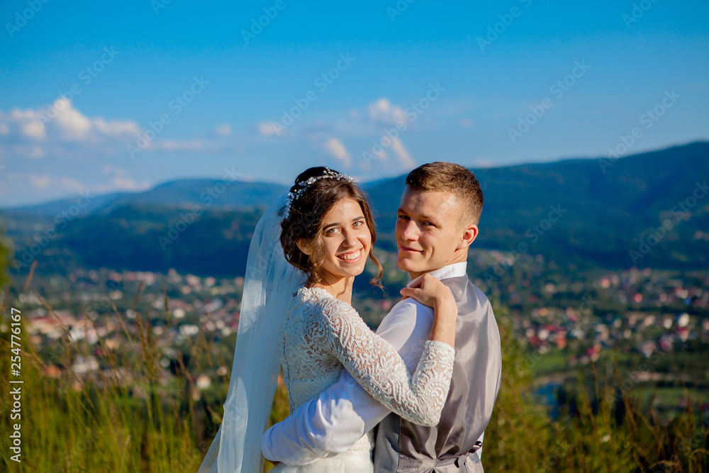 Newlyweds smile and hug each other among the meadow on top of the mountain. Wedding walk in the woods in the mountains, the gentle emotions of the couple, photo for Valentine's Day Newlyweds smile and hug each other among the meadow on top of the mountain. Wedding walk in the woods in the mountains, the gentle emotions of the couple, photo for Valentine's Day