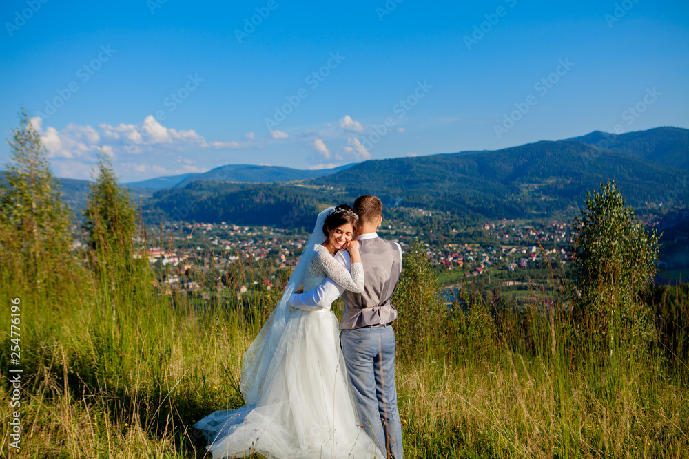 Newlyweds smile and hug each other among the meadow on top of the mountain. Wedding walk in the woods in the mountains, the gentle emotions of the couple, photo for Valentine's Day